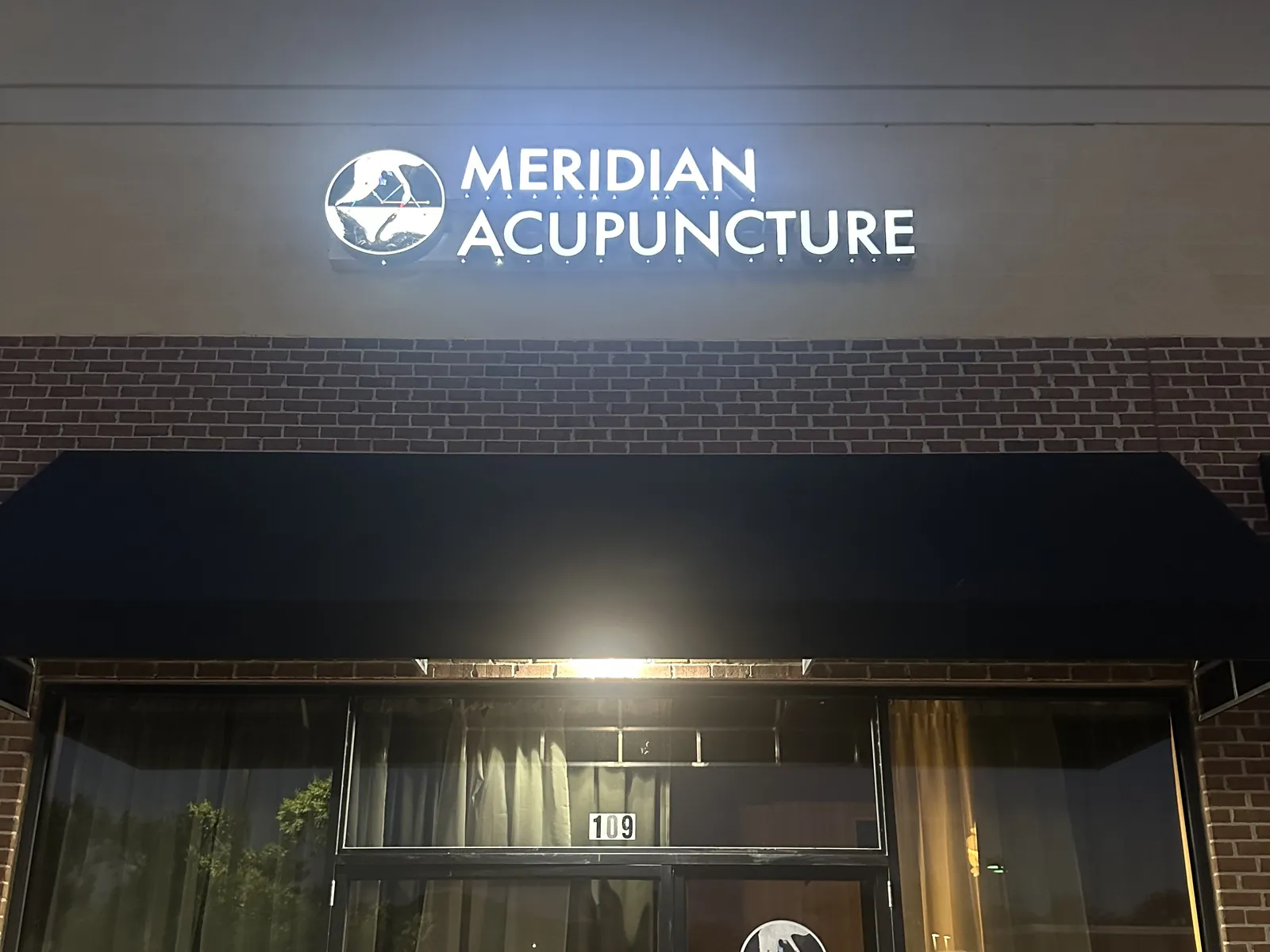 The Meridian Acupuncture storefront at 1731 Mallory Lane in Brentwood, with the illuminated sign above the entrance at dusk