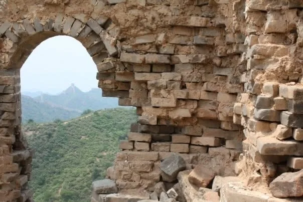 A view of green mountains through a weathered stone arch on the Great Wall of China