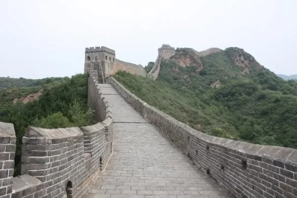 A stone path along the Great Wall of China winding over green hills