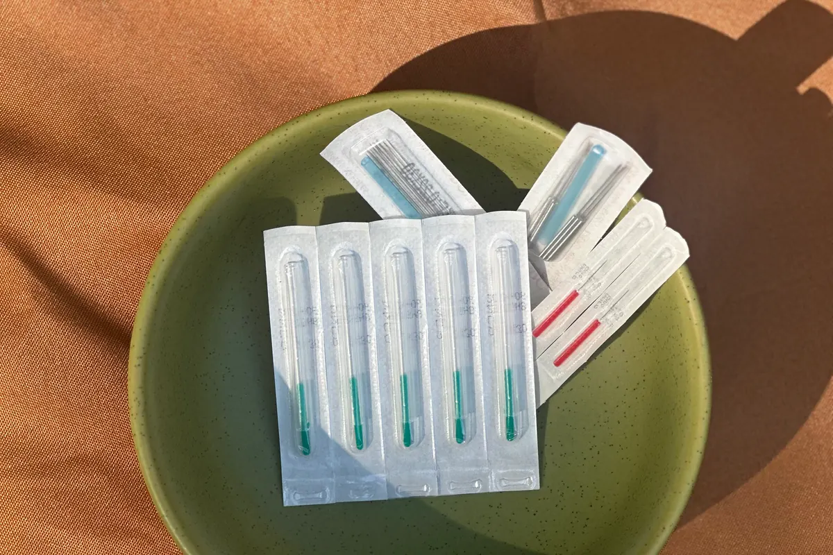Sealed single-use sterile acupuncture needles in a green ceramic bowl