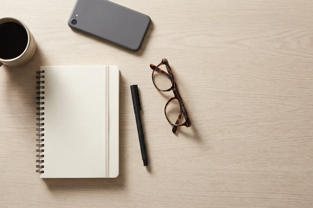 A desk with a notebook, pen, glasses, and phone, set up for a benefits call